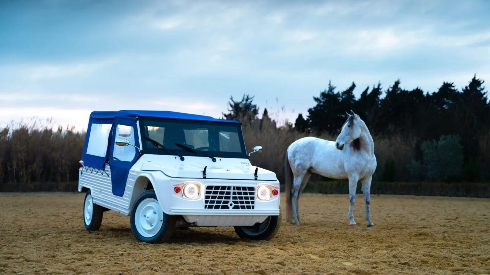 La eStory bianca con cappotta blu all'imbrunire, accanto a un cavallo bianco